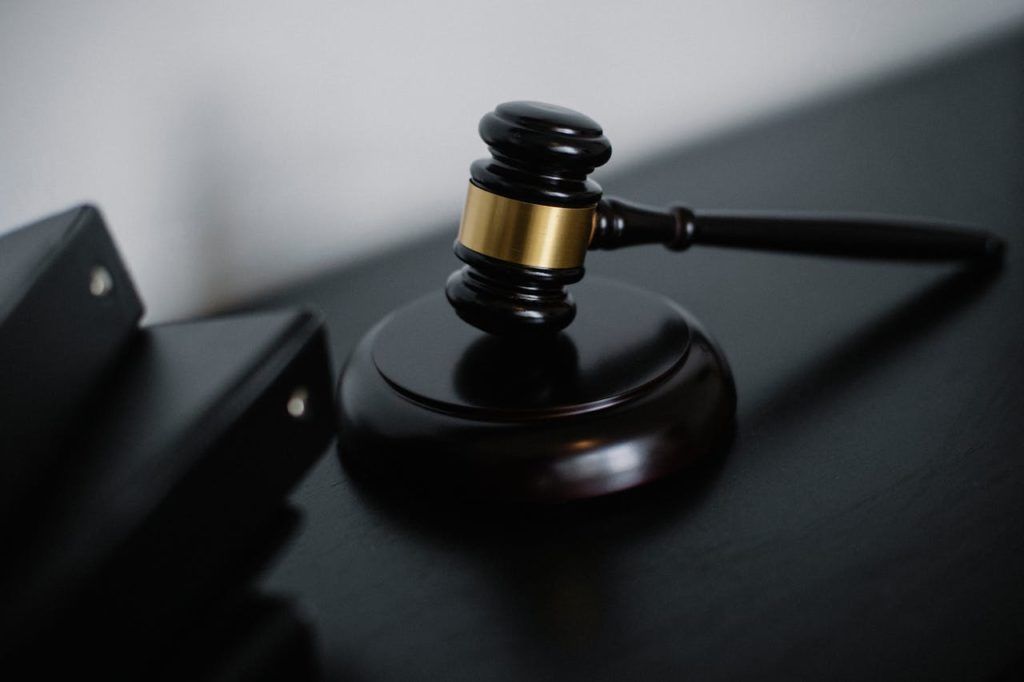 Gavel de madeira com detalhes dourados ao lado de pastas pretas.