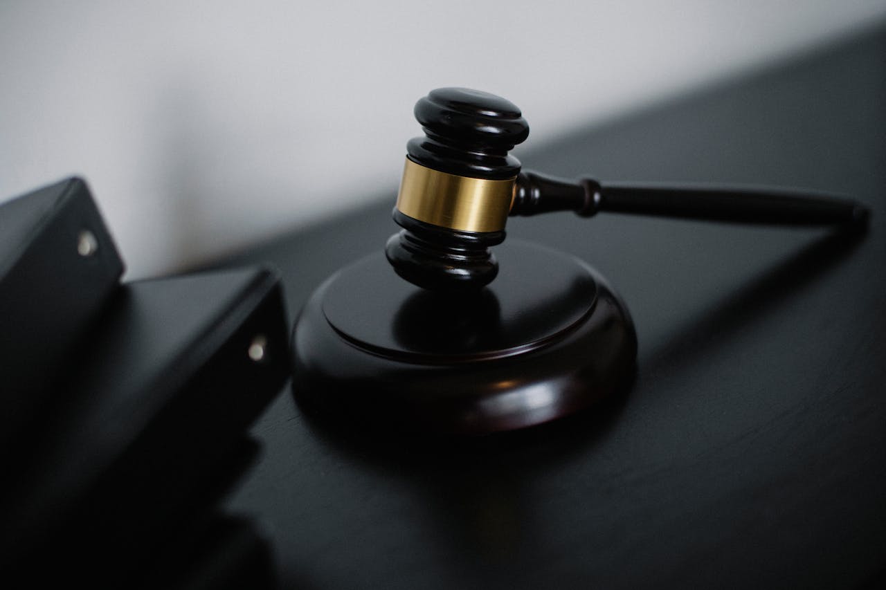 Gavel de madeira com detalhes dourados ao lado de pastas pretas.